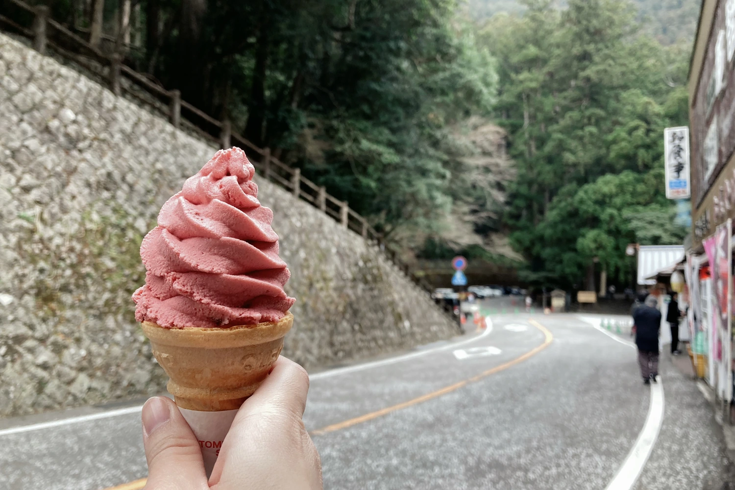 pink soft serve in a wafer cone, surrounded by trees