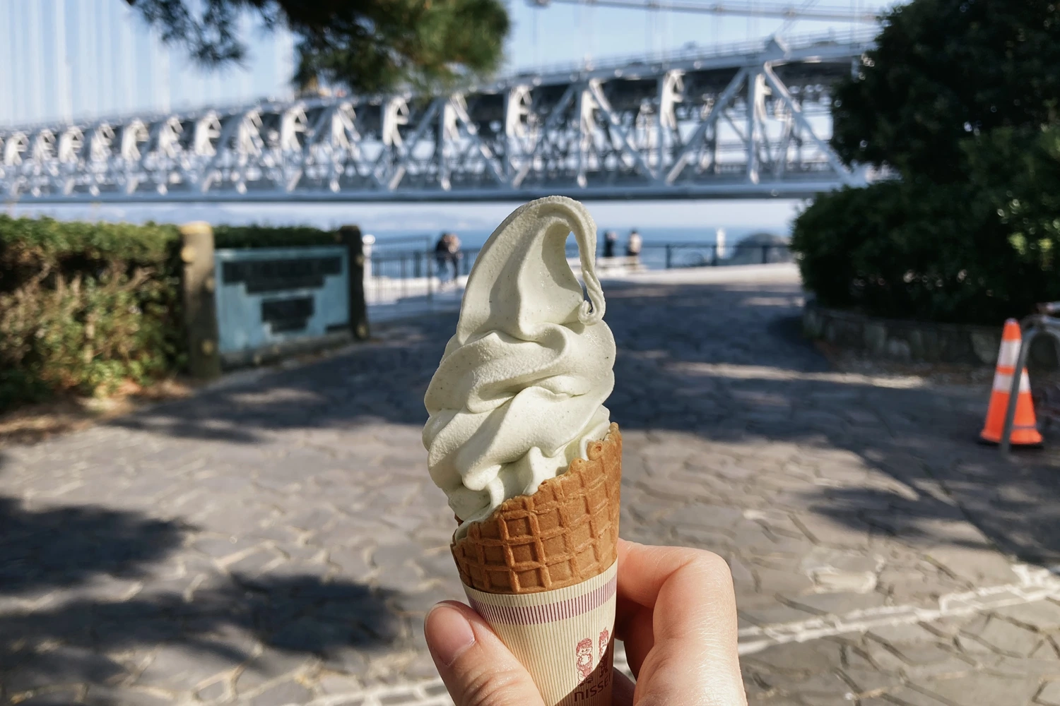 very light green soft serve in a waffle cone; a bridge nearby
