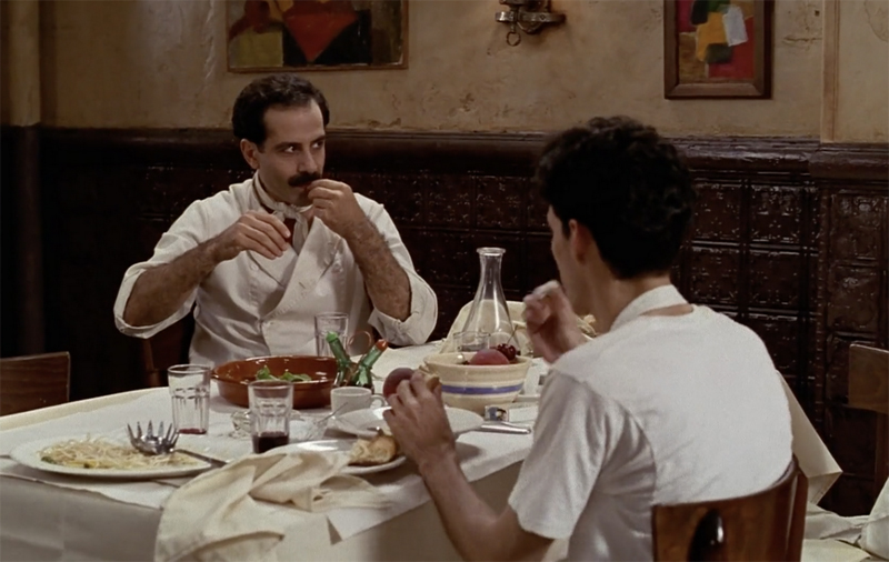 screenshot from the film 'big night'. two restaurant staff eat an improvised lunch at a table.