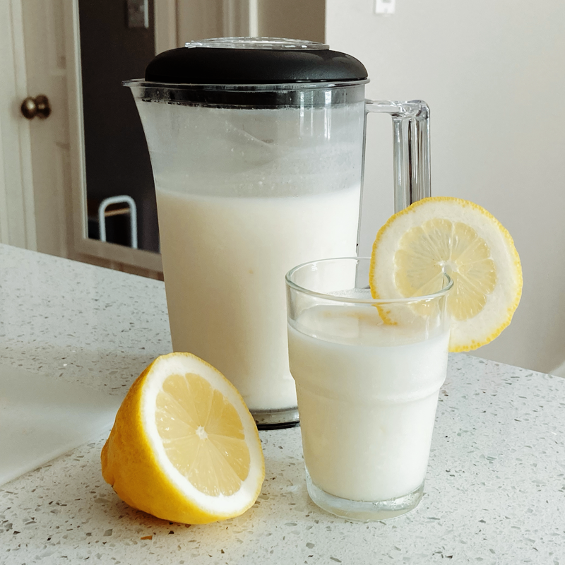 A glass and pitcher of thick and opaque lemonade, with sliced lemons for garnish.